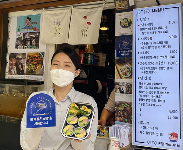 CJ제일제당 관계자가 메뉴에 스팸을 사용하는 ‘OTTO 김밥’ 앞에서 스팸 인증마크를 들어보이고 있다. 사진=CJ제일제당 제공